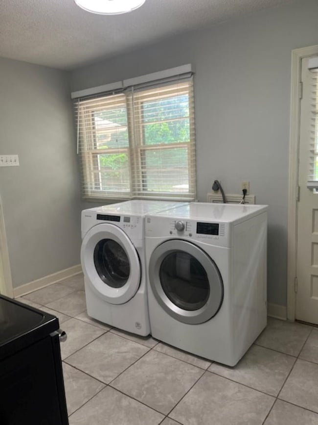 Laundry area featuring independent washer and dryer, a textured ceiling, light tile patterned floors, and baseboards