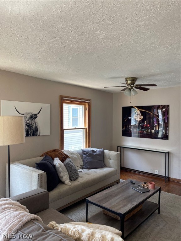 Living room with a textured ceiling, ceiling fan, and hardwood / wood-style floors