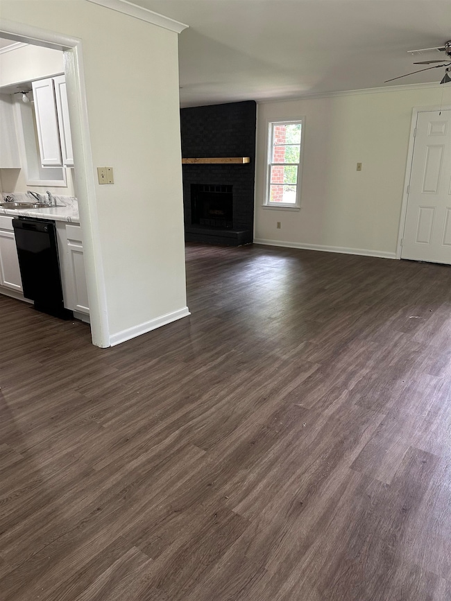 Unfurnished living room with dark wood-style floors, crown molding, a fireplace, and a ceiling fan