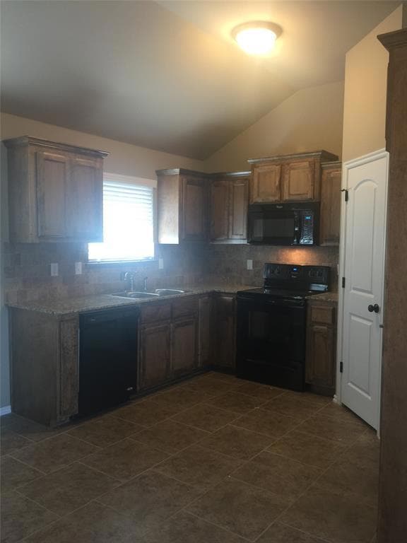 Kitchen with black appliances, tasteful backsplash, vaulted ceiling, and dark tile patterned floors