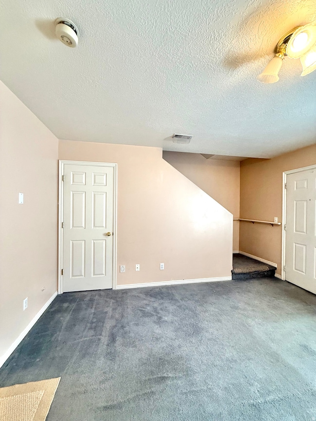 Unfurnished room featuring dark colored carpet, a textured ceiling, and a smoke detector