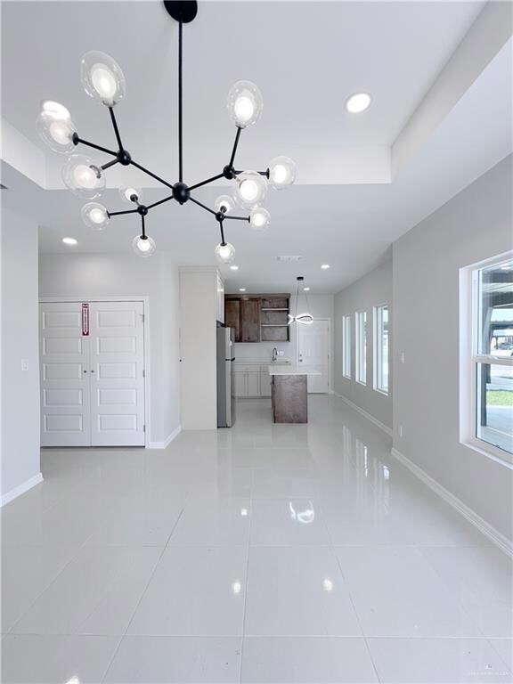 Unfurnished living room featuring a sink, a chandelier, recessed lighting, baseboards, and light tile patterned floors