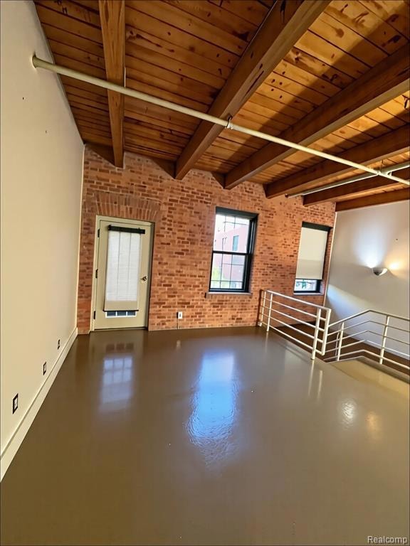 Bonus room with concrete flooring, brick wall, and a wooden ceiling with exposed beams