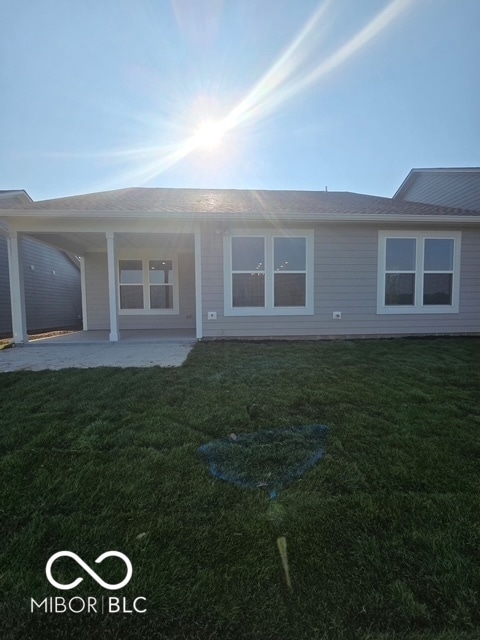 back of house with a yard, a shingled roof, and a patio