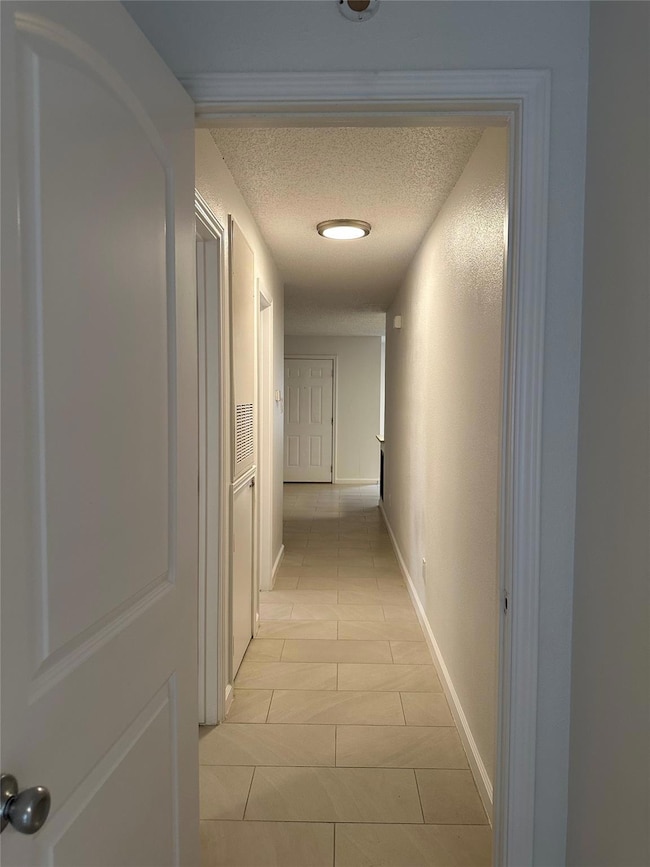 Hallway with a textured ceiling, light tile patte