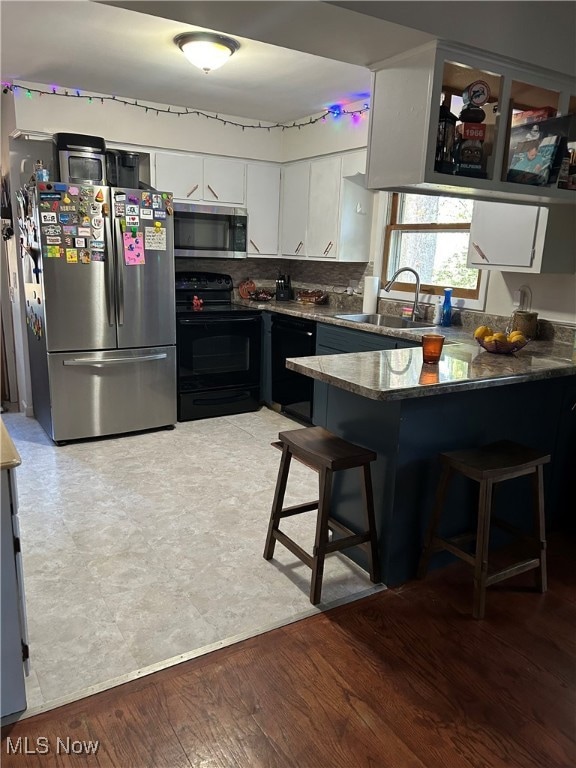 Kitchen featuring white cabinets, a kitchen breakfast bar, black appliances, a peninsula, and light wood-type flooring
