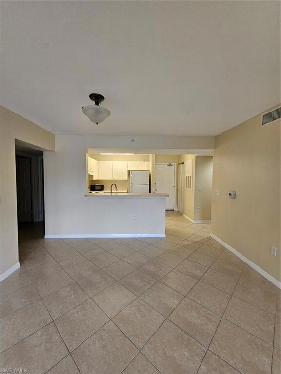Empty room featuring ceiling fan, light tile patterned flooring, light colored carpet, visible vents, and baseboards