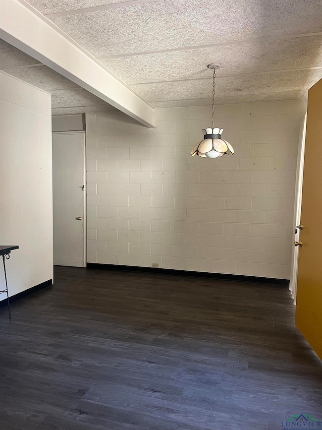 Unfurnished room featuring concrete block wall and dark wood-style flooring