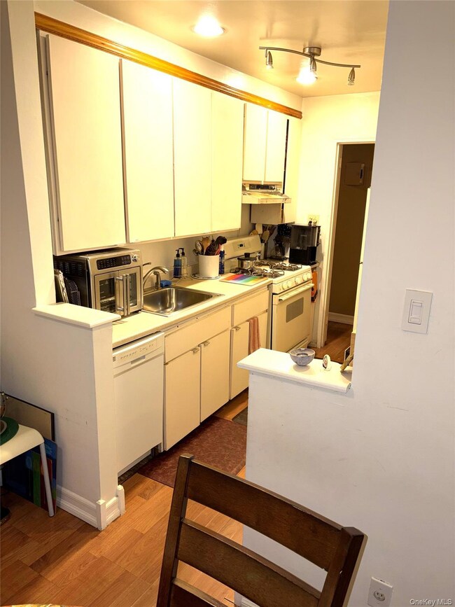 Kitchen with white appliances, light wood-style flooring, light countertops, under cabinet range hood, and white cabinetry