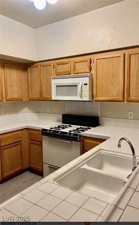 Kitchen featuring white appliances, a sink, tile c