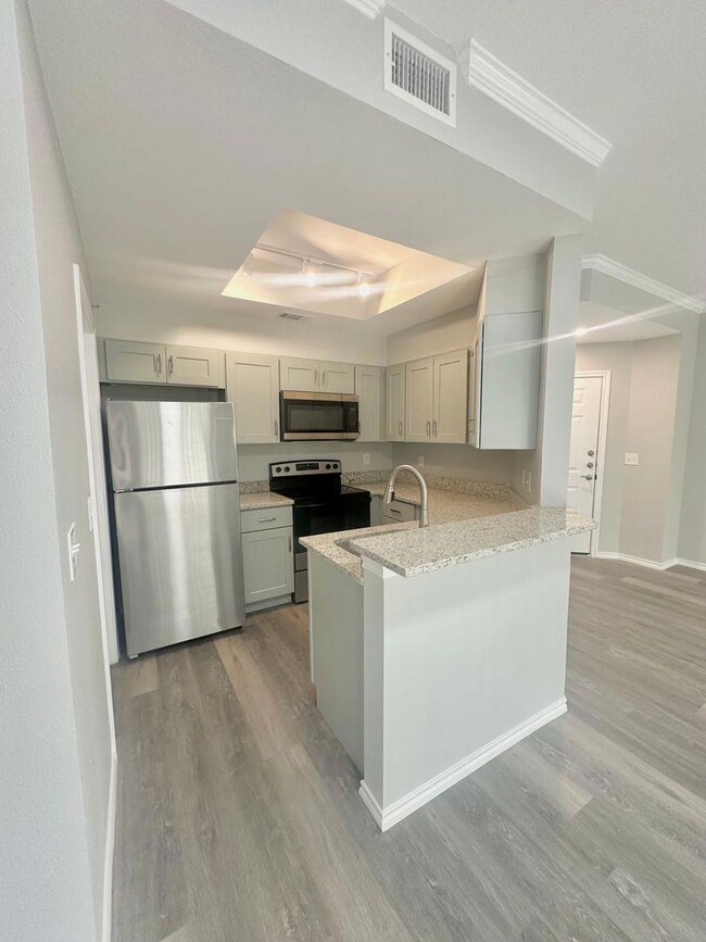 Kitchen with stainless steel appliances, light stone counters, light wood-style flooring, and a raised ceiling