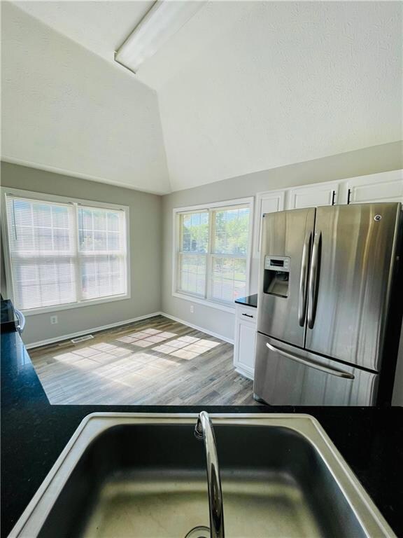 Kitchen with stainless steel refrigerator with ice dispenser, white cabinets, dark countertops, vaulted ceiling, and wood finished floors