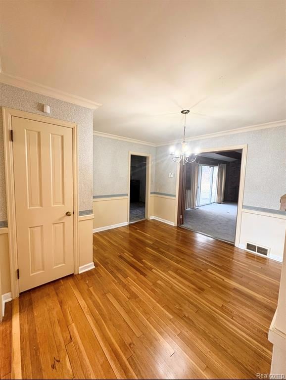 Unfurnished dining area with light wood finished floors, crown molding, a chandelier, and wallpapered walls