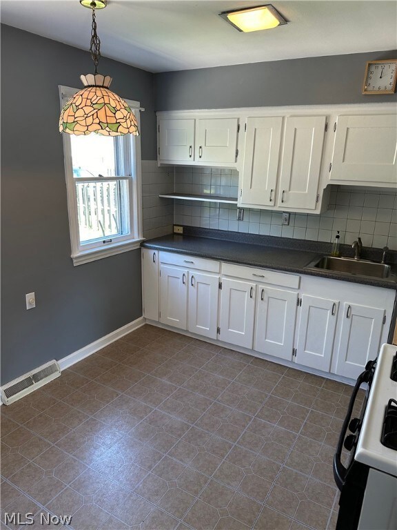 Kitchen featuring hanging light fixtures, a wealth of natural light, dark tile flooring, and backsplash