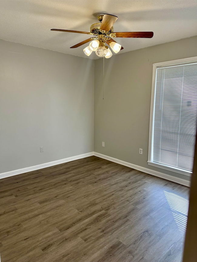 Empty room with dark wood-style flooring, a ceiling fan, and baseboards