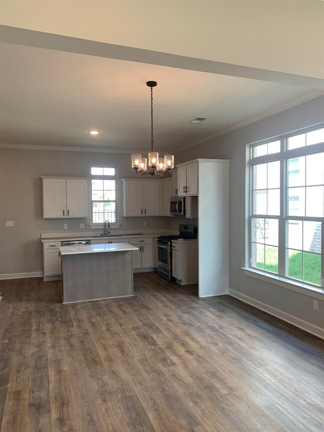 Kitchen with appliances with stainless steel finishes, ornamental molding, a chandelier, LVP wood flooring, solid surface countertops