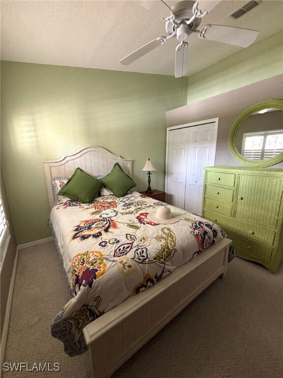Carpeted bedroom with a textured ceiling, visible vents, baseboards, a ceiling fan, and a closet