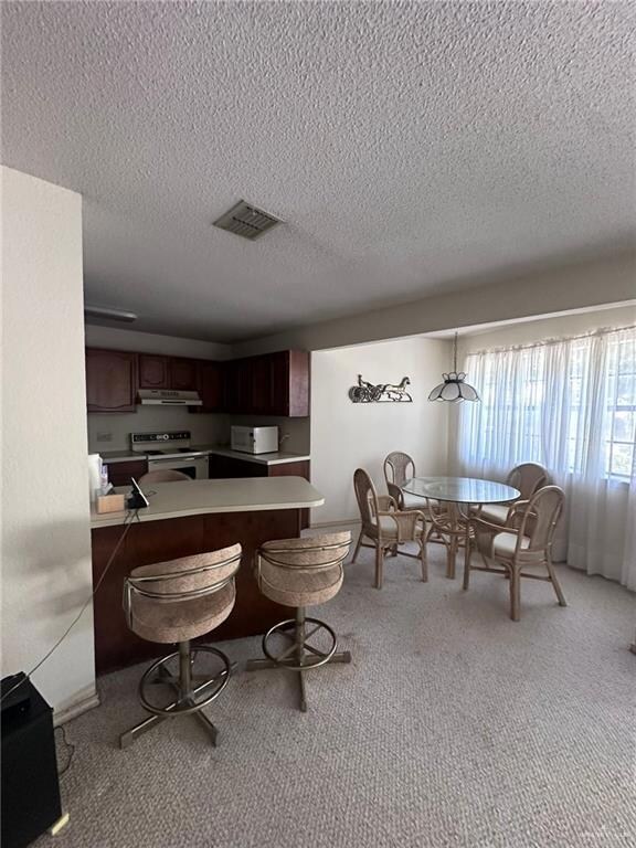 Kitchen with a breakfast bar, white appliances, light carpet, decorative light fixtures, and kitchen peninsula