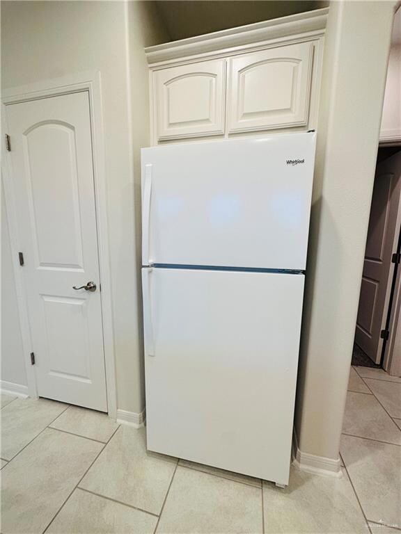 Kitchen featuring white cabinets, white refrigerator, and light tile floors