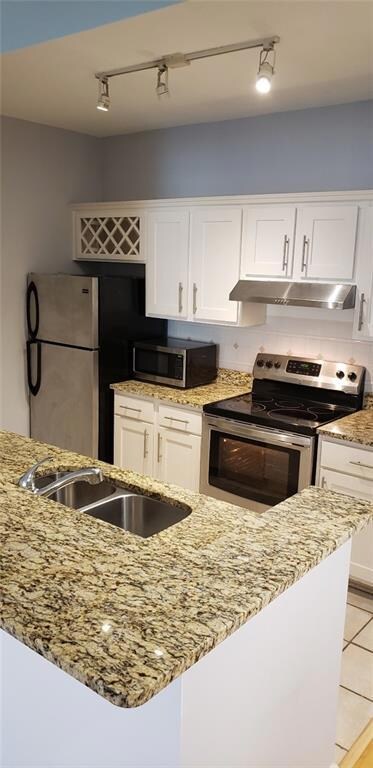 Kitchen with appliances with stainless steel finishes, under cabinet range hood, white cabinets, light stone countertops, and decorative backsplash