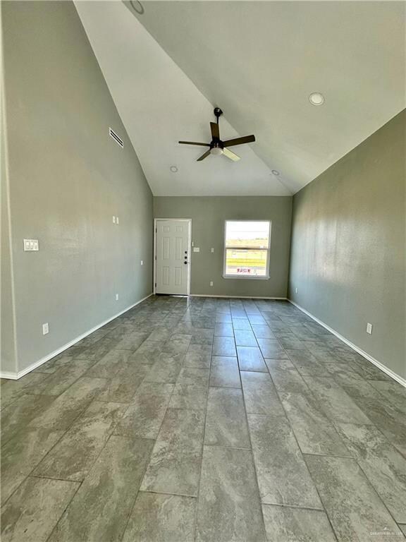 Tiled empty room with vaulted ceiling and ceiling fan