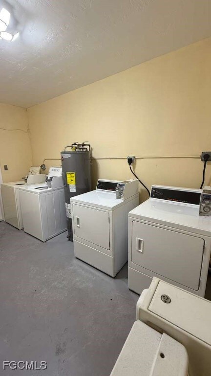 Washroom with independent washer and dryer, unfinished concrete floors, electric water heater, and a textured ceiling