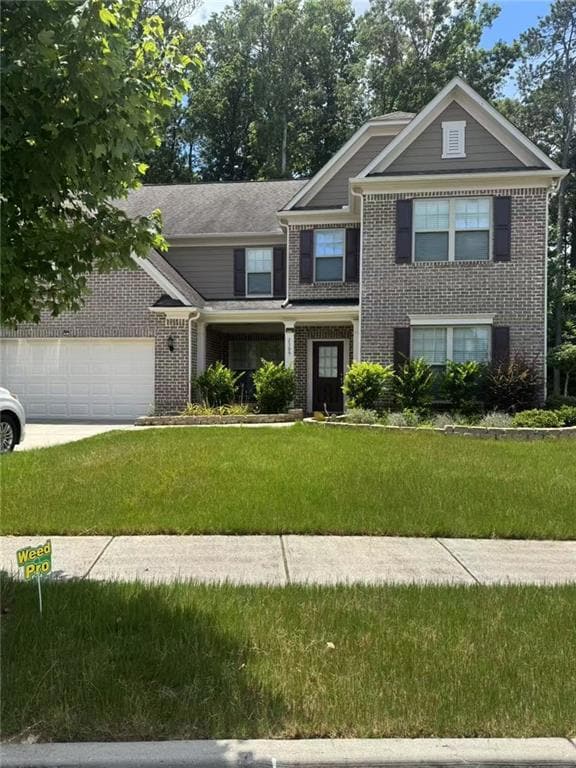 View of front of house with brick siding, a front lawn, an attached garage, and driveway
