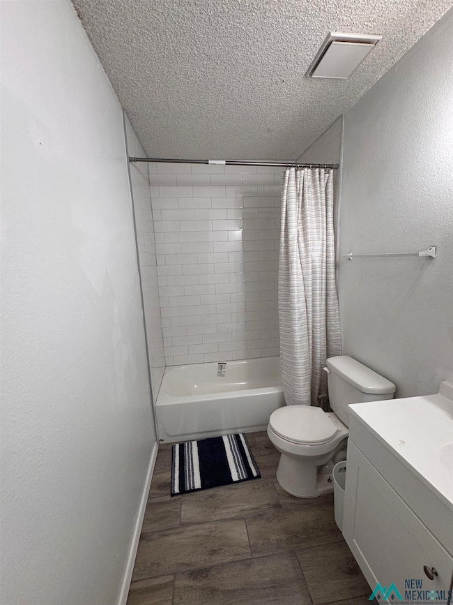 Full bath featuring shower / bath combo with shower curtain, vanity, dark wood-style floors, a textured ceiling, and a textured wall