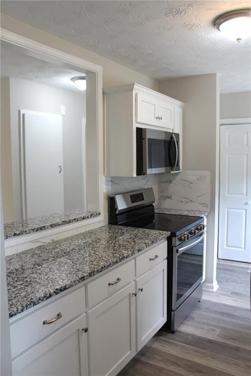 Kitchen with stainless steel appliances, dark wood finished floors, white cabinetry, light stone counters, and a textured ceiling