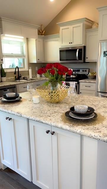 Kitchen with stainless steel appliances, light stone countertops, vaulted ceiling, and white cabinetry