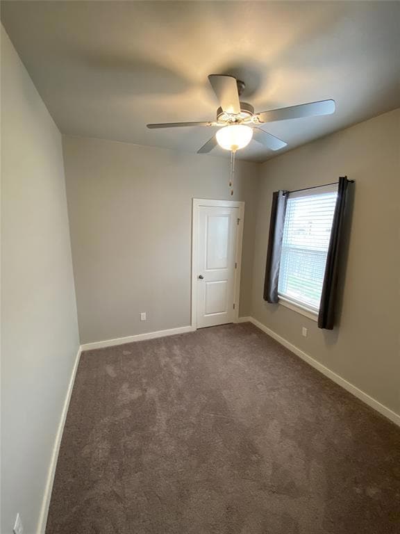 Empty room with dark carpet, ceiling fan, and base