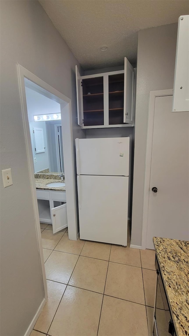 Kitchen with freestanding refrigerator, light tile patterned floors, white cabinetry, light stone countertops, and a textured ceiling