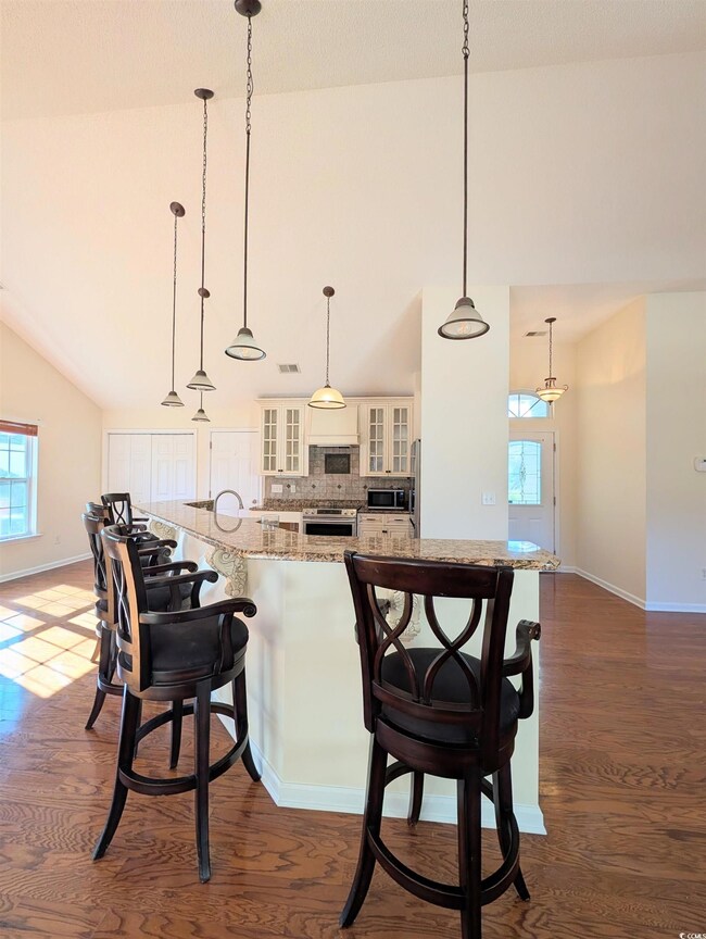 Kitchen featuring glass insert cabinets, light stone countertops, a kitchen breakfast bar, decorative backsplash, and high vaulted ceiling