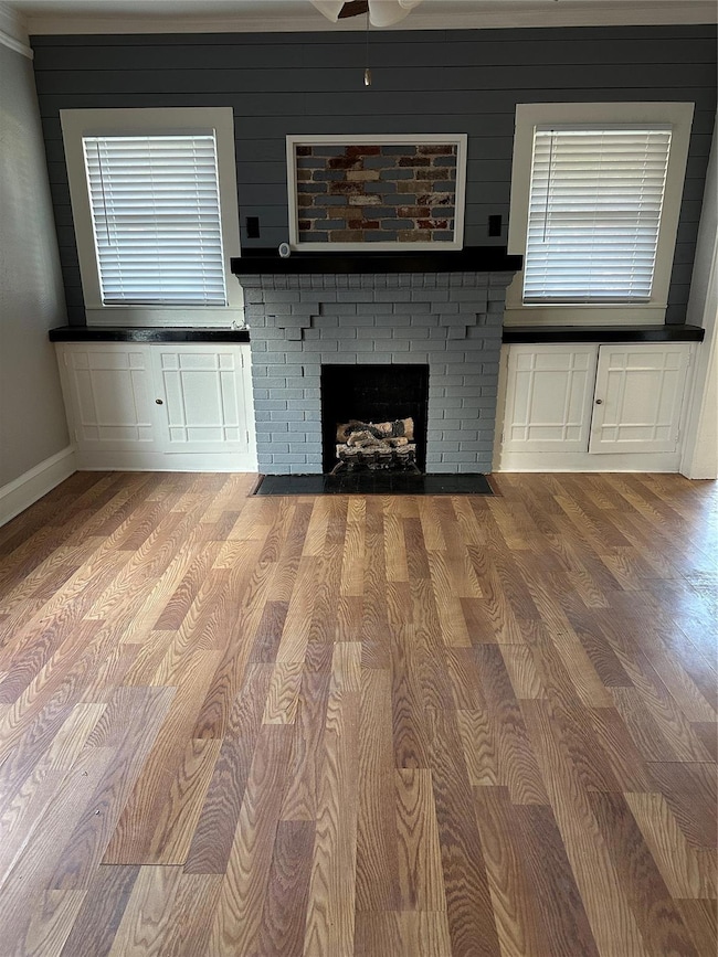 Unfurnished living room with wood finished floors, baseboards, and a brick fireplace