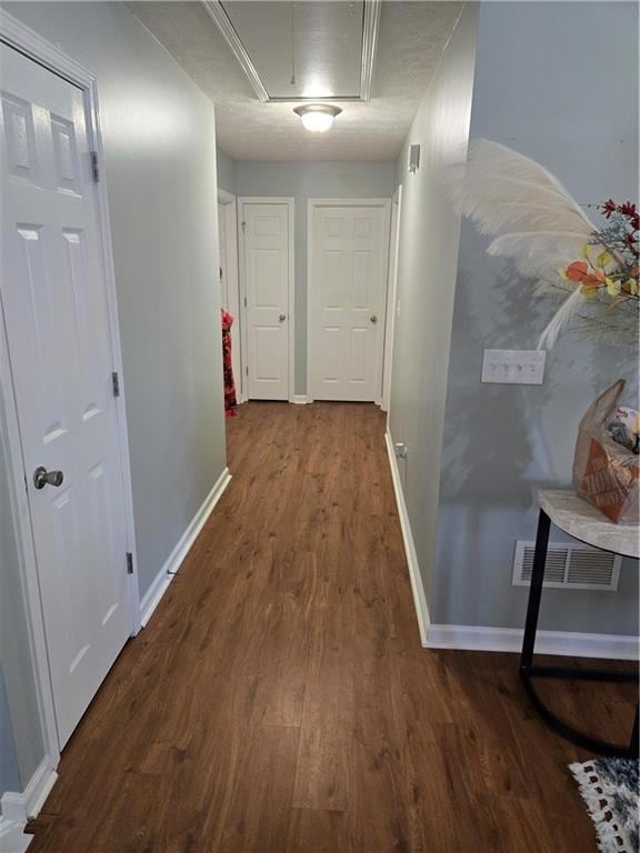 Hallway featuring dark wood-style flooring, visible vents, baseboards, and attic access