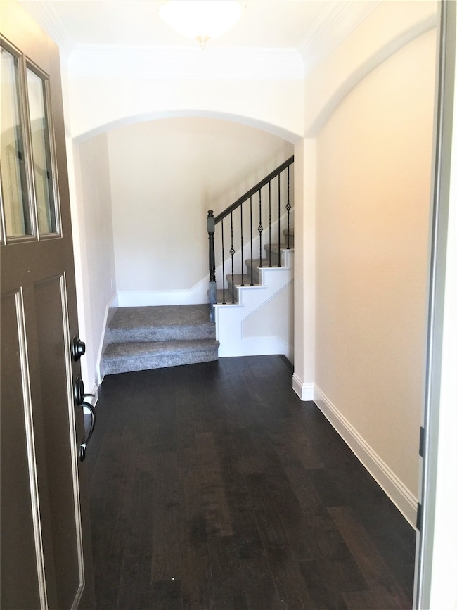 Foyer with stairs, dark wood finished floors, ornamental molding, and arched walkways