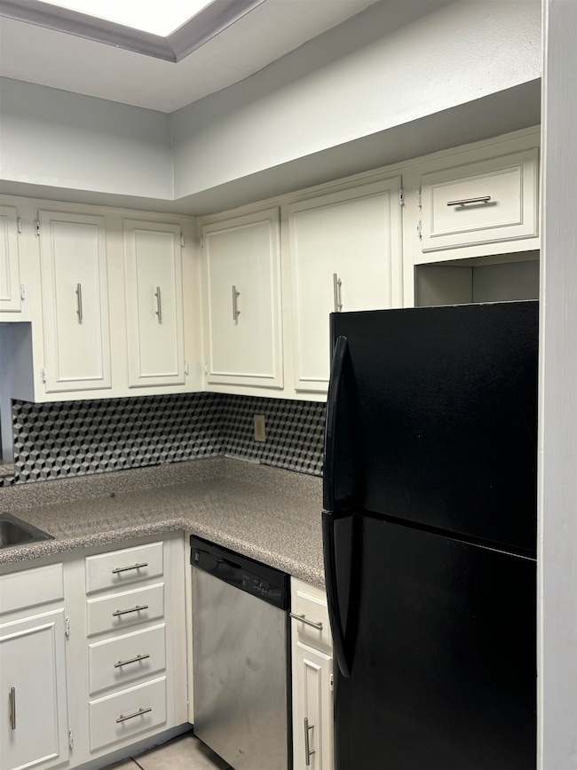 Kitchen featuring freestanding refrigerator, dishwasher, backsplash, and white cabinetry