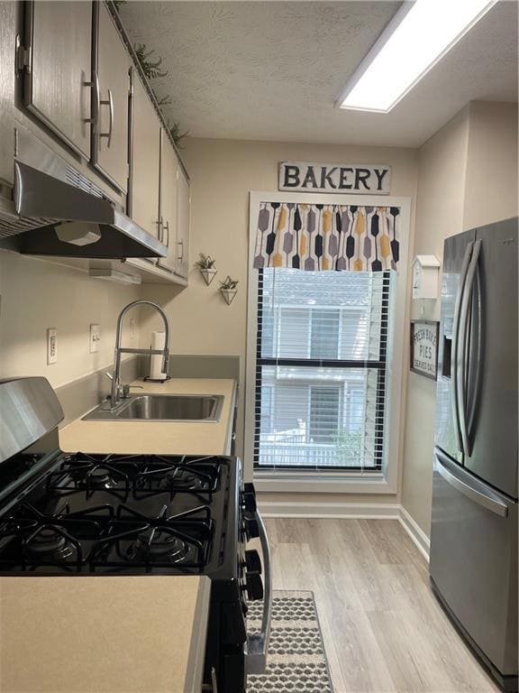 Kitchen featuring stove, fridge, exhaust hood, light wood finished floors, and a textured ceiling