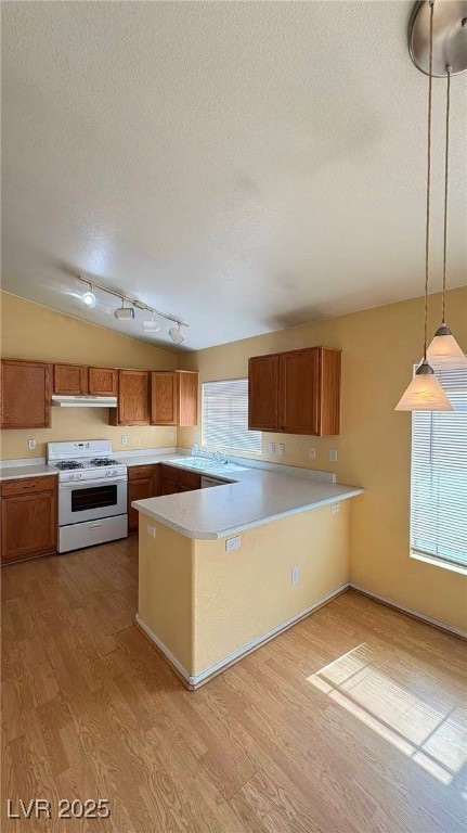 Kitchen featuring light countertops, brown cabinets, hanging light fixtures, white range with gas stovetop, and a peninsula