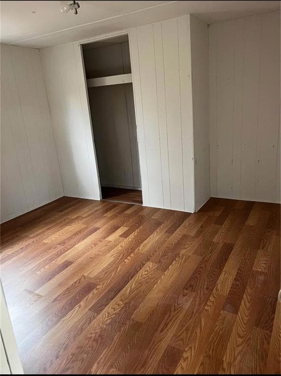 Unfurnished bedroom with wood finished floors, wooden walls, and a closet