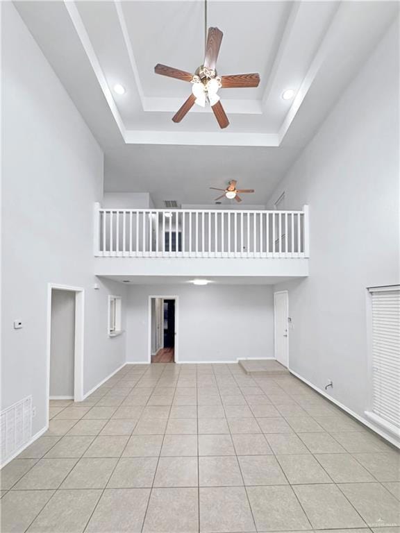 Unfurnished living room with ceiling fan, a towering ceiling, a tray ceiling, and light tile patterned floors