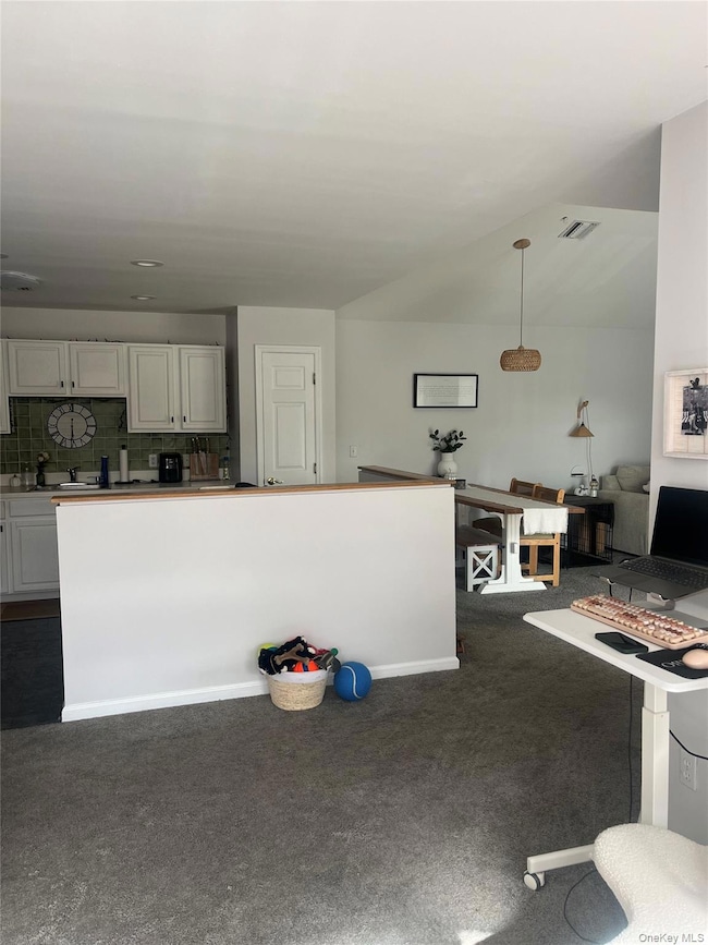 Kitchen with backsplash, white cabinetry, dark carpet, and hanging light fixtures