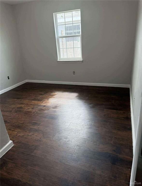 Spare room featuring baseboards and dark wood-style floors