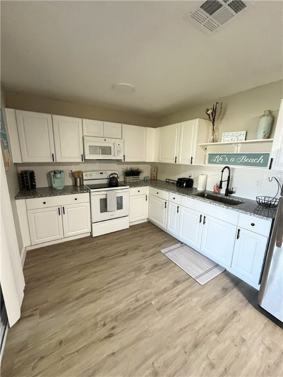 Kitchen featuring white appliances, white cabinets, light wood finished floors, dark stone counters, and open shelves