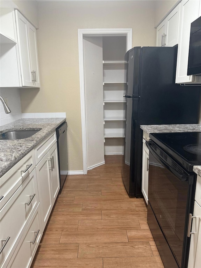 Kitchen with black appliances, white cabinets, light stone countertops, and light wood finished floors