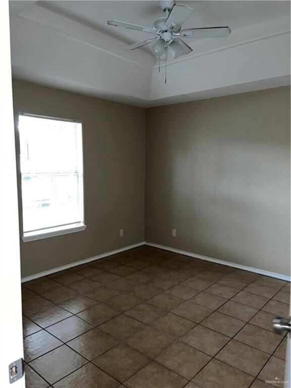 Empty room with a tray ceiling, baseboards, and a ceiling fan