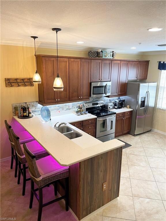 Kitchen featuring a peninsula, stainless steel appliances, a kitchen bar, ornamental molding, and light stone counters