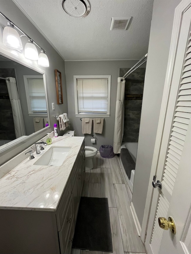 Full bath with a textured ceiling, vanity, wood finish floors, and shower / bath combo
