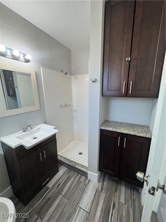 Full bathroom featuring vanity, a textured wall, a shower stall, dark wood-style flooring, and a textured ceiling