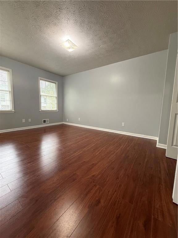 Empty room with dark wood-type flooring and a textured ceiling